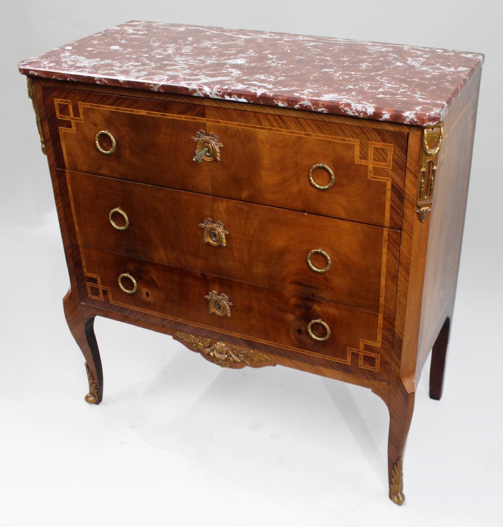 A French Louis XVI style mahogany and tulipwood three-drawer commode featuring geometric inlay, ormolu mounts, and a red mottled marble top.