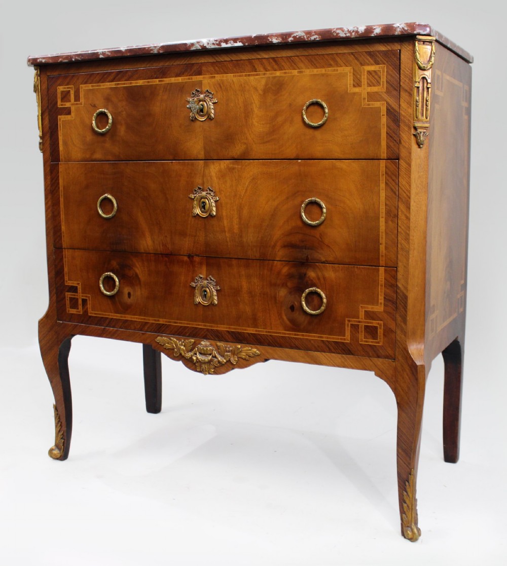 A French Louis XVI style mahogany and tulipwood three-drawer commode featuring geometric inlay, ormolu mounts, and a red mottled marble top. View IV