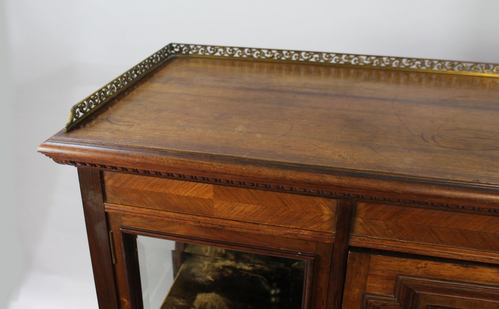 Late Victorian rosewood display cabinet featuring a central inlaid floral door, two glass side doors, a brass gallery rail top, and a lower tier shelf on turned legs. View III
