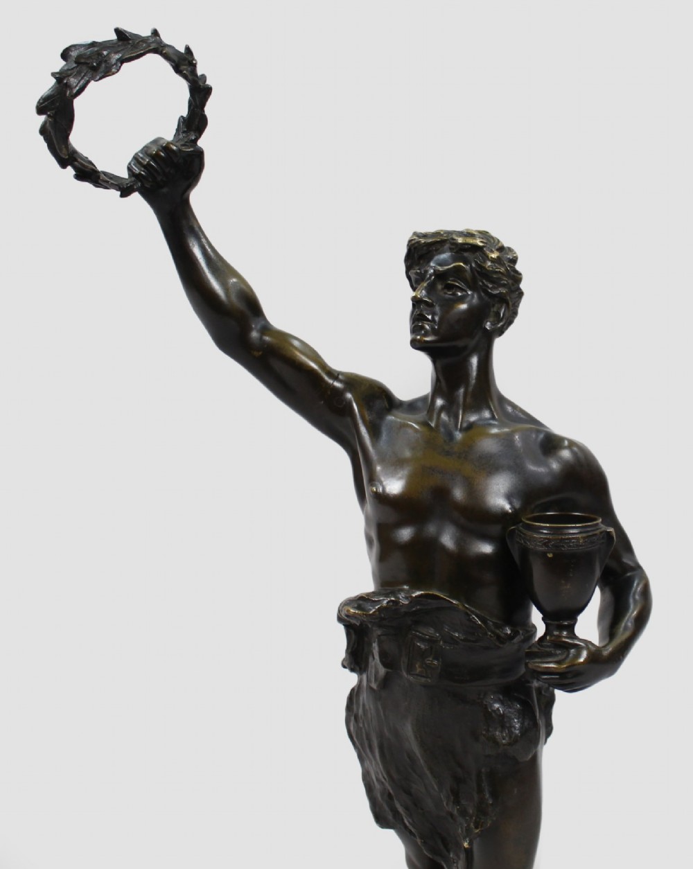 A dark brown patinated bronze figure of a classical male standing on a rocky base, holding a chalice in one hand and raising a laurel wreath aloft in the other. View XII
