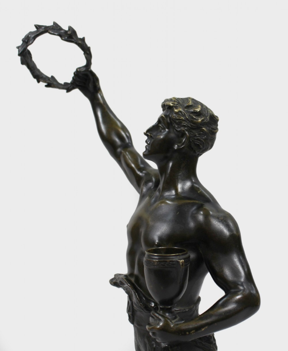 A dark brown patinated bronze figure of a classical male standing on a rocky base, holding a chalice in one hand and raising a laurel wreath aloft in the other. View XIII