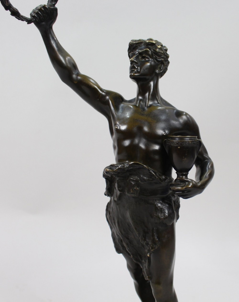 A dark brown patinated bronze figure of a classical male standing on a rocky base, holding a chalice in one hand and raising a laurel wreath aloft in the other. View XIV