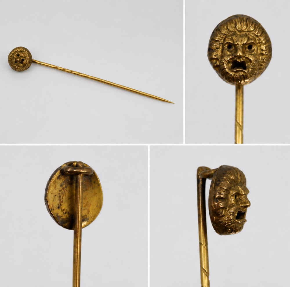 An antique Victorian gold stick pin featuring a relief-carved classical mask head atop a slender twisted shaft.