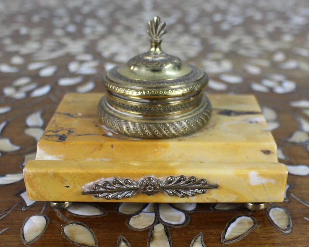 A rectangular yellow Siena marble desk inkstand featuring a central patterned ormolu inkpot with a finial lid, a front brass leaf applique, and small turned metal feet. View II