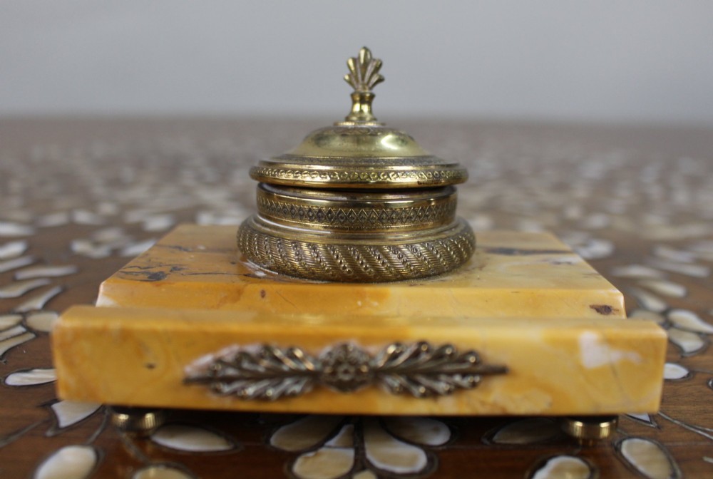 A rectangular yellow Siena marble desk inkstand featuring a central patterned ormolu inkpot with a finial lid, a front brass leaf applique, and small turned metal feet. View III