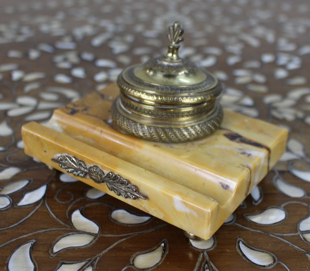A rectangular yellow Siena marble desk inkstand featuring a central patterned ormolu inkpot with a finial lid, a front brass leaf applique, and small turned metal feet. View IV