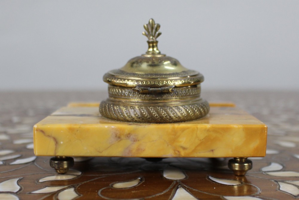 A rectangular yellow Siena marble desk inkstand featuring a central patterned ormolu inkpot with a finial lid, a front brass leaf applique, and small turned metal feet. View V