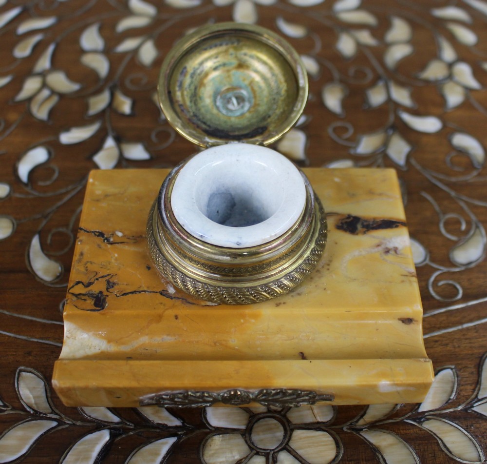 A rectangular yellow Siena marble desk inkstand featuring a central patterned ormolu inkpot with a finial lid, a front brass leaf applique, and small turned metal feet. View VI