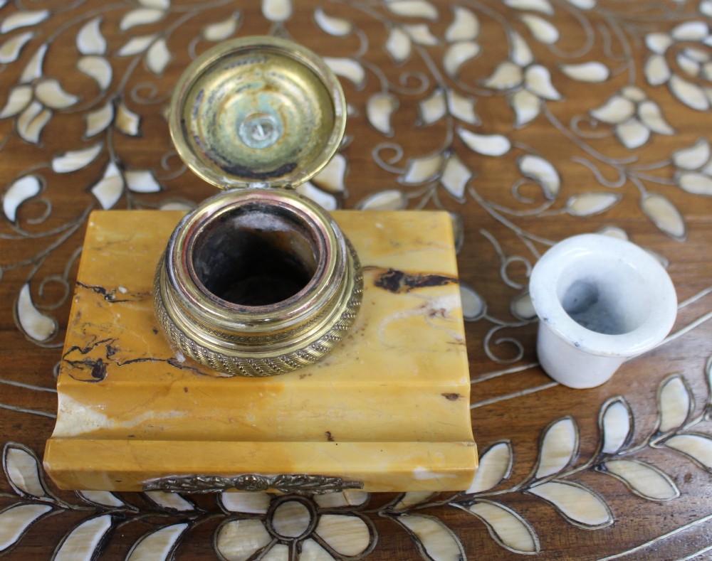 A rectangular yellow Siena marble desk inkstand featuring a central patterned ormolu inkpot with a finial lid, a front brass leaf applique, and small turned metal feet. View VII