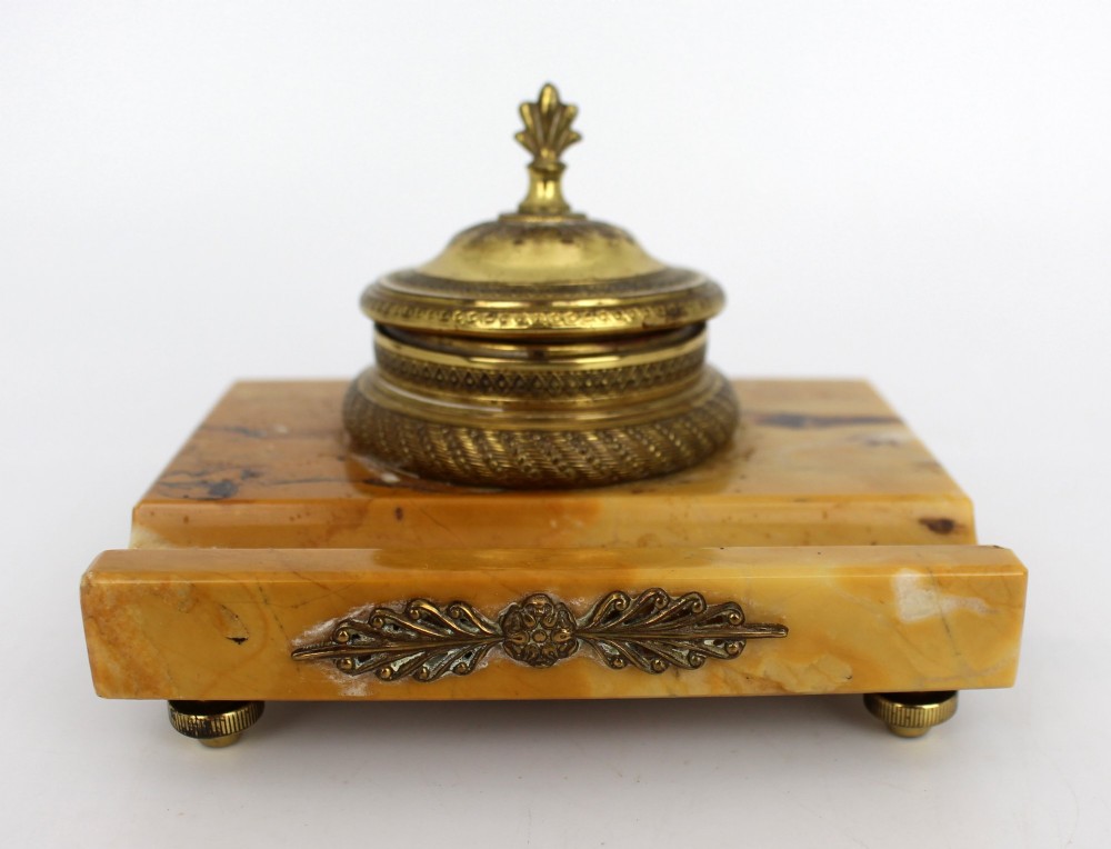 A rectangular yellow Siena marble desk inkstand featuring a central patterned ormolu inkpot with a finial lid, a front brass leaf applique, and small turned metal feet. View VIII