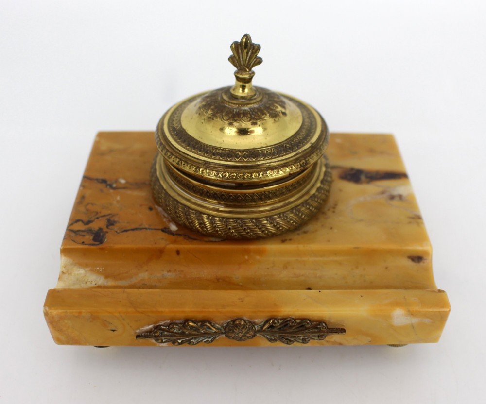 A rectangular yellow Siena marble desk inkstand featuring a central patterned ormolu inkpot with a finial lid, a front brass leaf applique, and small turned metal feet. View IX
