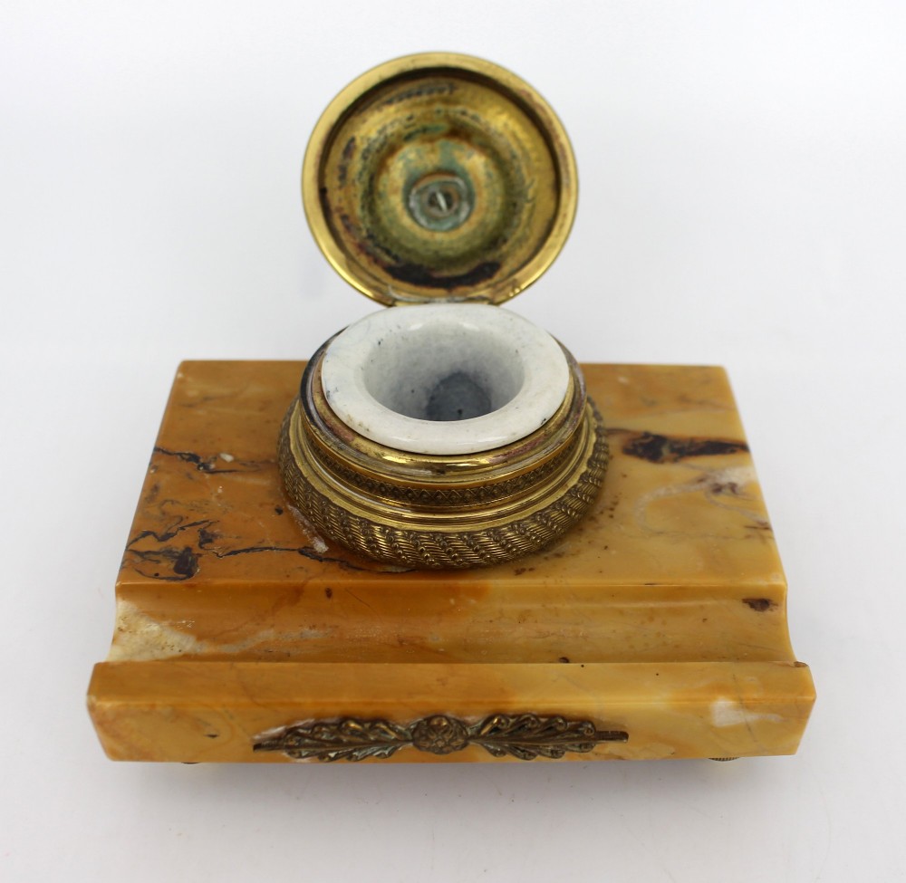 A rectangular yellow Siena marble desk inkstand featuring a central patterned ormolu inkpot with a finial lid, a front brass leaf applique, and small turned metal feet. View X