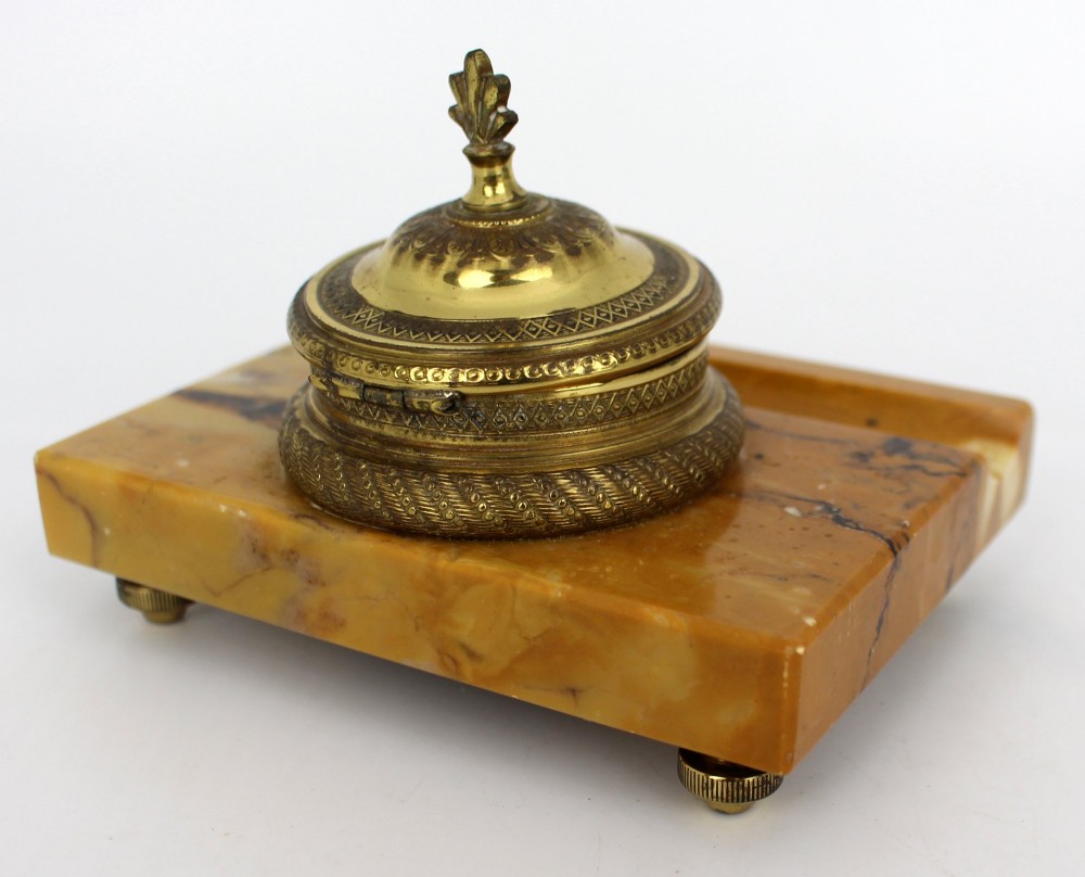 A rectangular yellow Siena marble desk inkstand featuring a central patterned ormolu inkpot with a finial lid, a front brass leaf applique, and small turned metal feet. View XI
