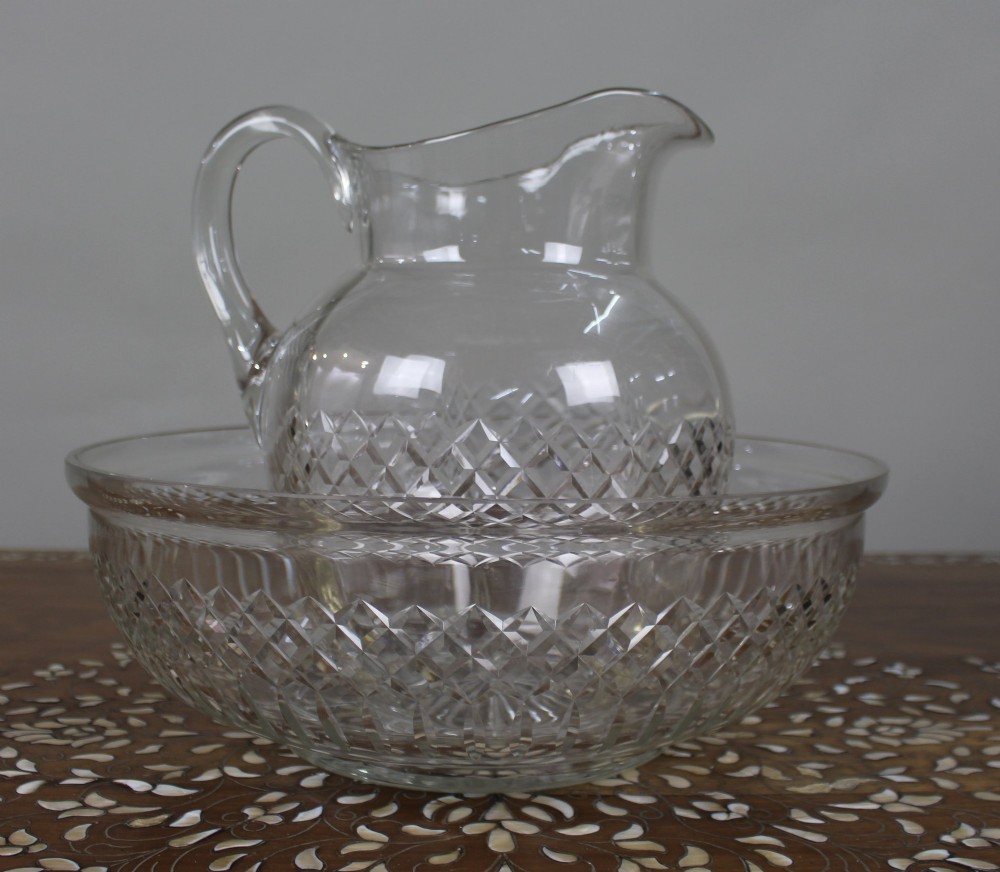 A clear cut crystal jug featuring a diamond motif seated inside a matching large round cut crystal basin.