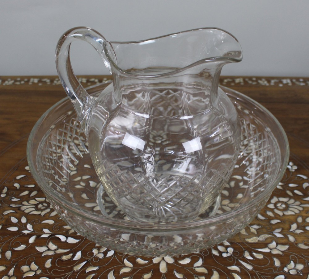 A clear cut crystal jug featuring a diamond motif seated inside a matching large round cut crystal basin. View II