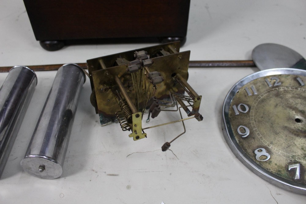 An Art Deco dark oak longcase clock case featuring a domed hood and glazed door alongside an unmounted brass movement, pendulum, chrome dial, and three cylindrical weights. View IV