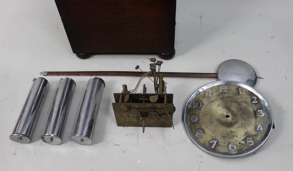 An Art Deco dark oak longcase clock case featuring a domed hood and glazed door alongside an unmounted brass movement, pendulum, chrome dial, and three cylindrical weights. View VII