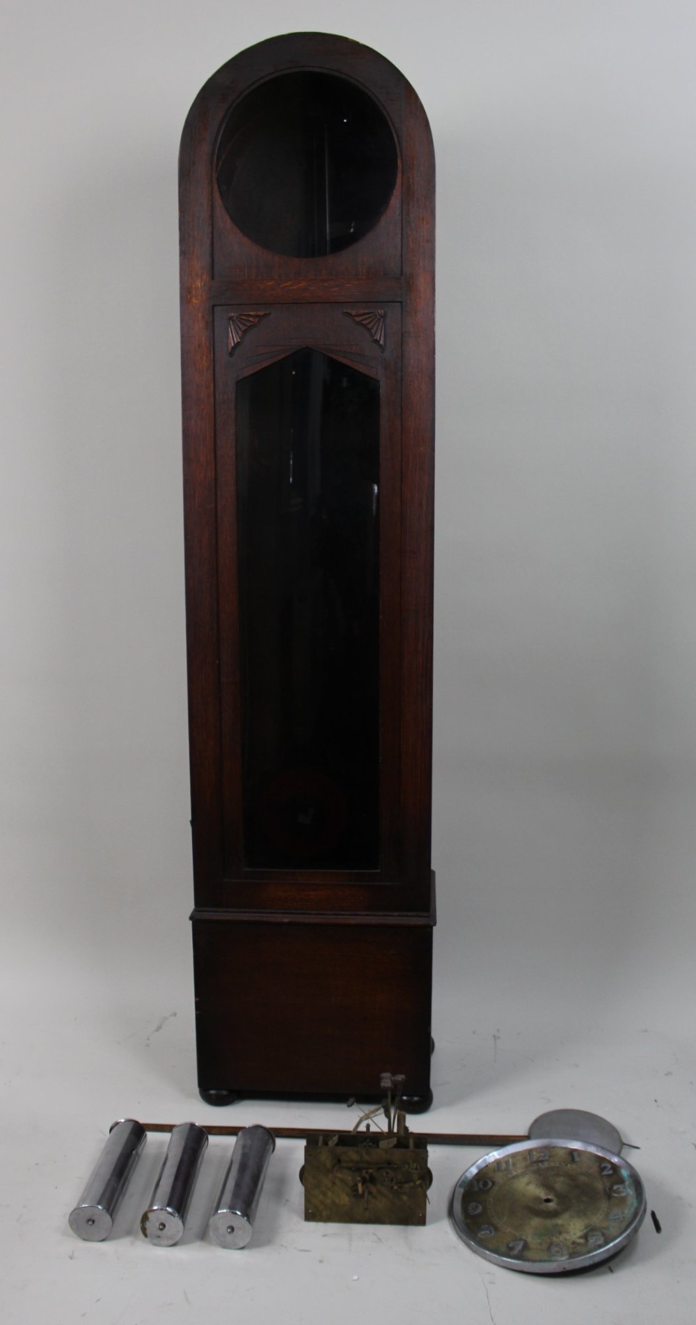 An Art Deco dark oak longcase clock case featuring a domed hood and glazed door alongside an unmounted brass movement, pendulum, chrome dial, and three cylindrical weights. View VIII