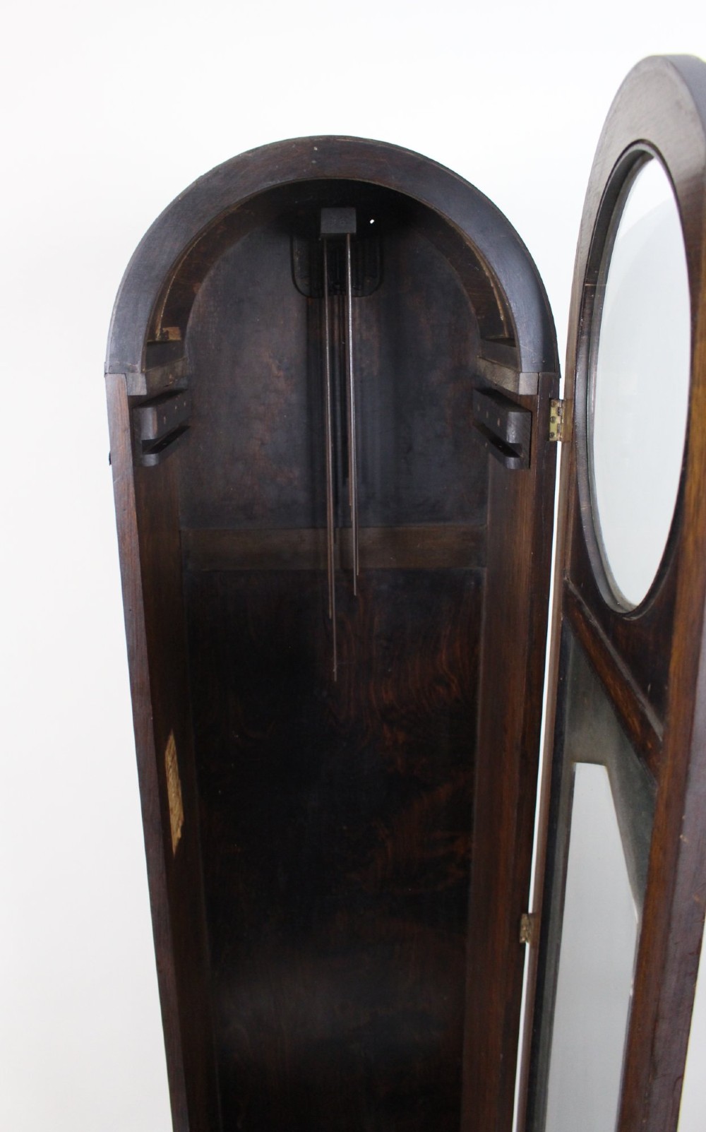 An Art Deco dark oak longcase clock case featuring a domed hood and glazed door alongside an unmounted brass movement, pendulum, chrome dial, and three cylindrical weights. View IX
