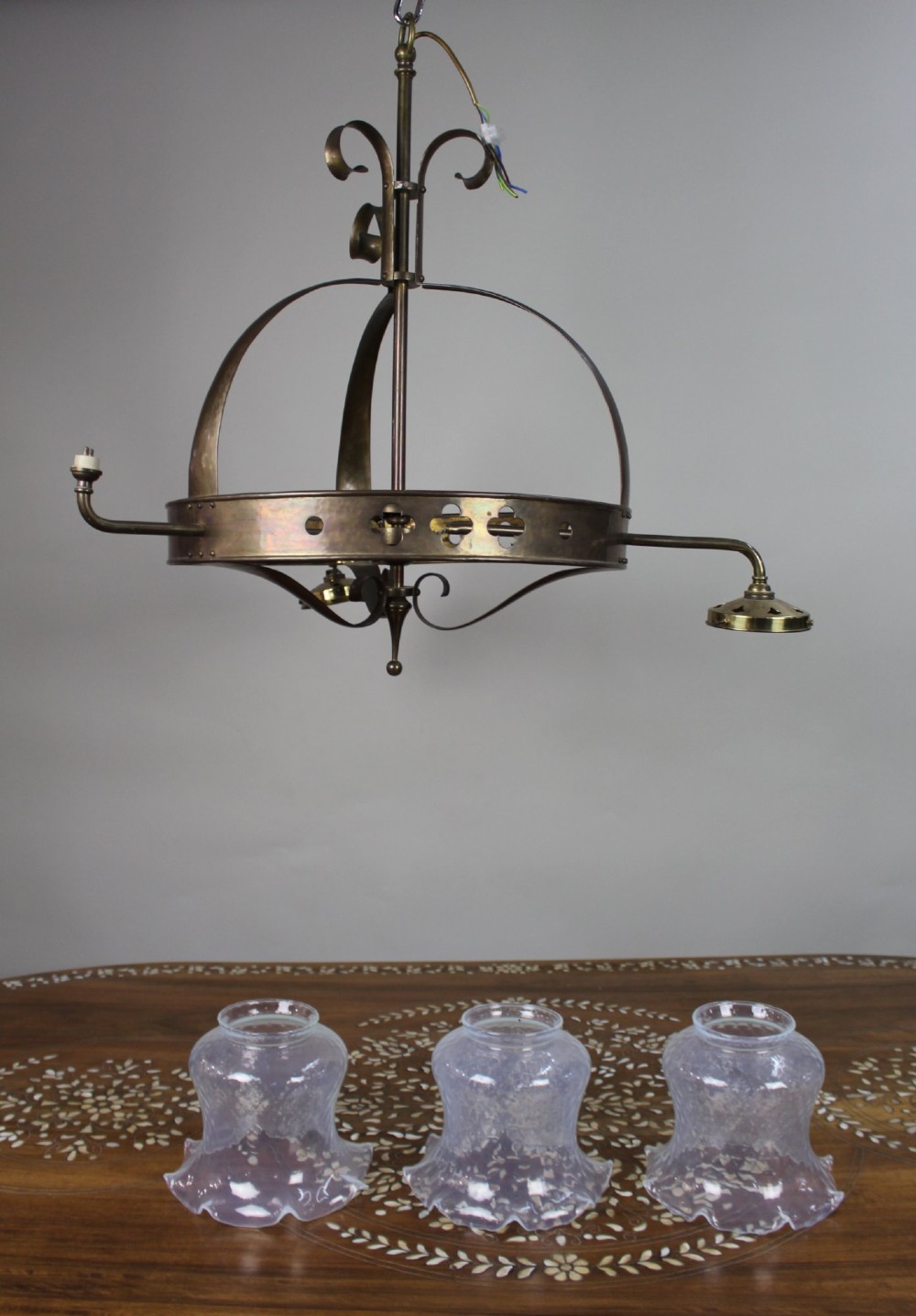 A Victorian Gothic Revival brass three-light gasolier frame featuring an arched cage and pierced trefoil band, presented alongside three ruffled opalescent glass shades.