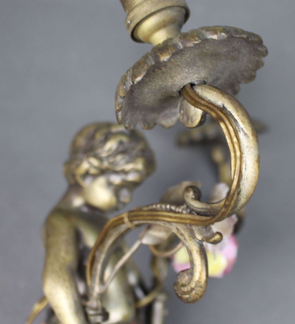 A pair of cast metal wall sconces featuring sculpted cherubs holding twin scroll arms decorated with ceramic floral motifs and electrical light sockets. View VII