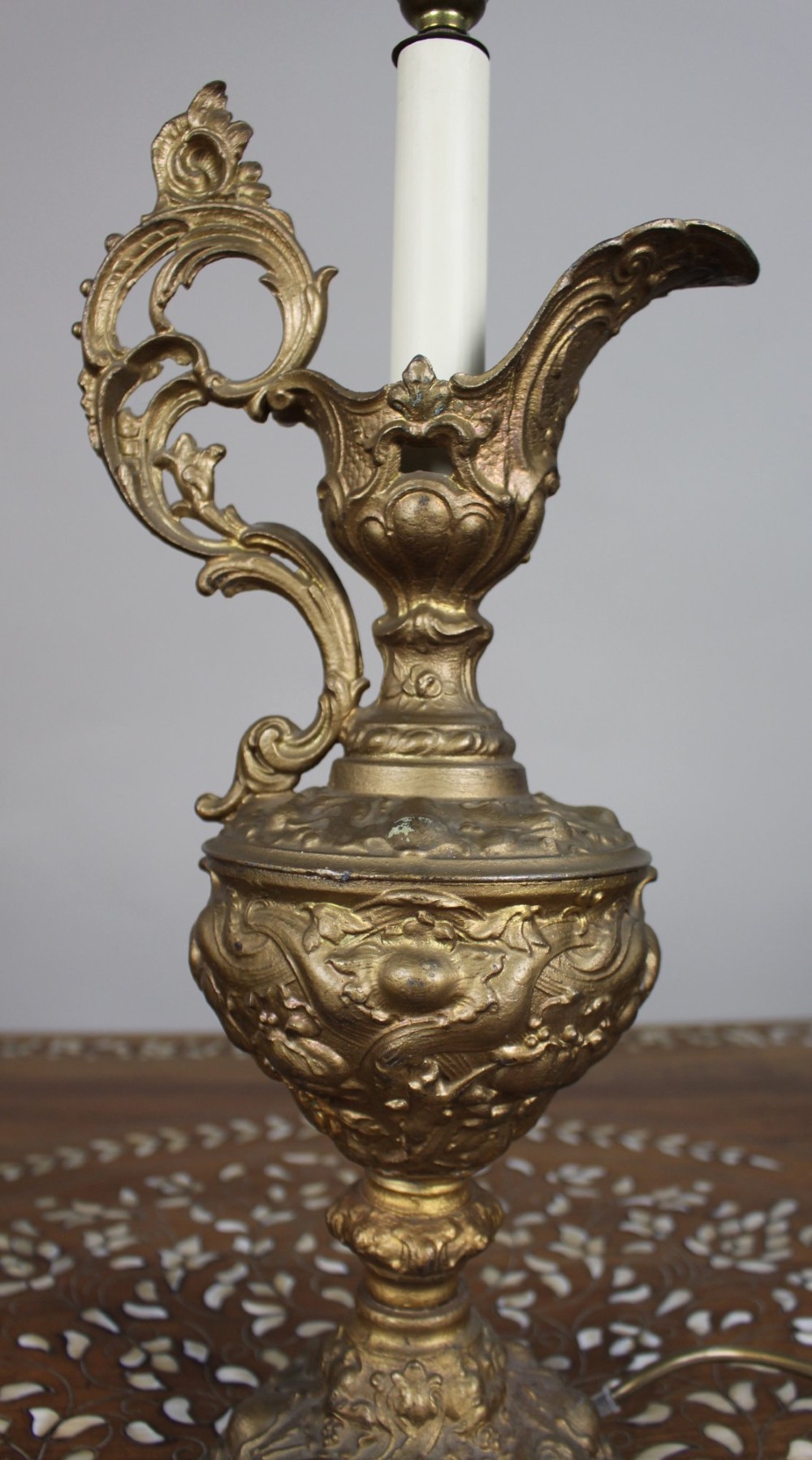 An ornate antique gilt metal table lamp fashioned in the shape of a Rococo ewer with a scrolled handle and intricate leaf relief patterns. View II