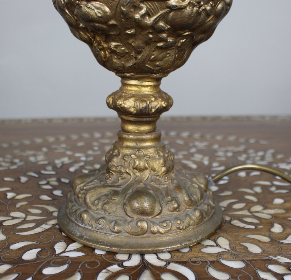 An ornate antique gilt metal table lamp fashioned in the shape of a Rococo ewer with a scrolled handle and intricate leaf relief patterns. View III