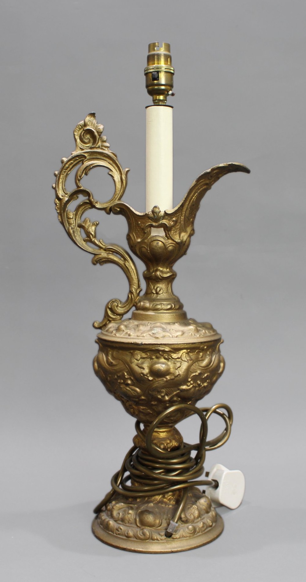 An ornate antique gilt metal table lamp fashioned in the shape of a Rococo ewer with a scrolled handle and intricate leaf relief patterns. View VII