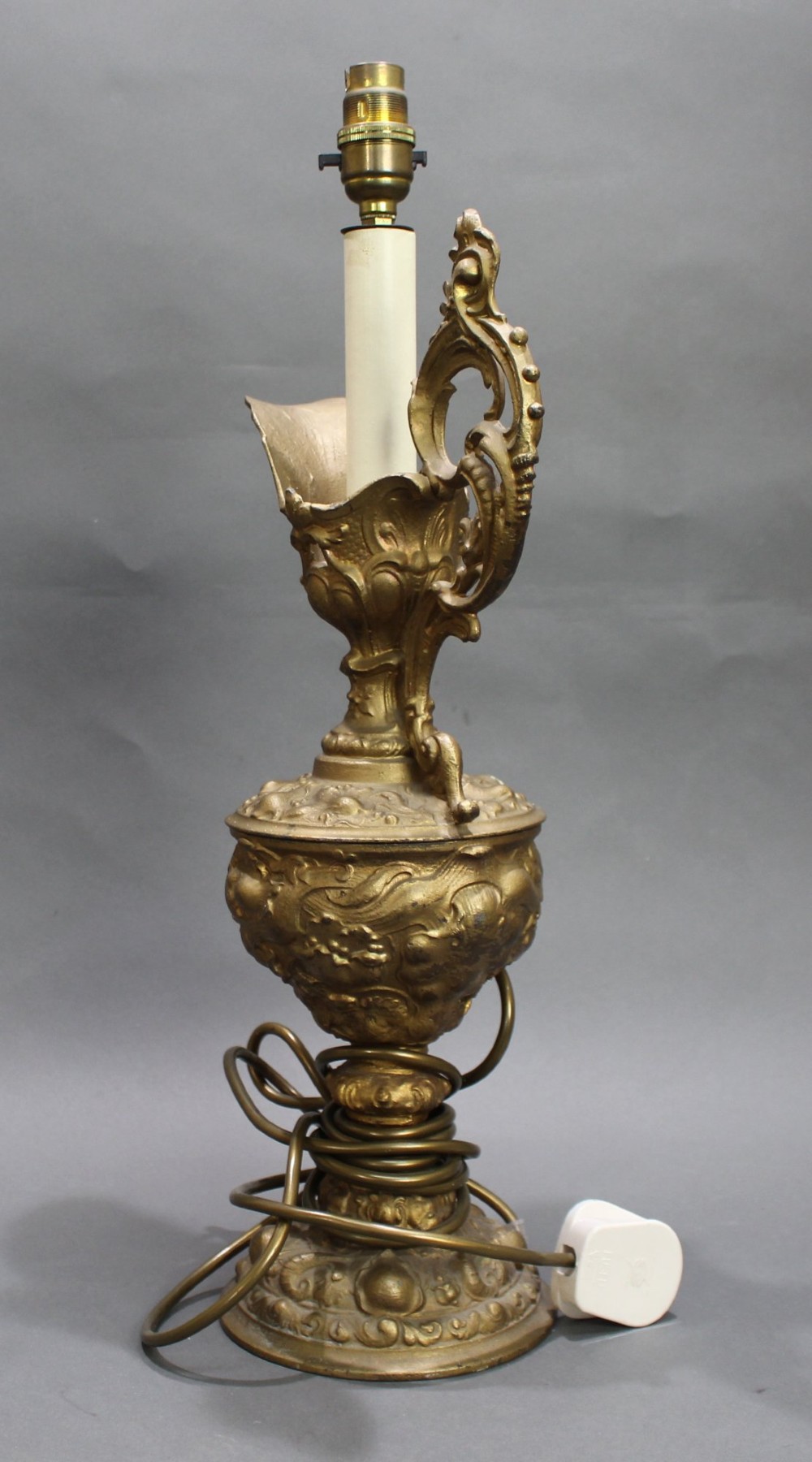 An ornate antique gilt metal table lamp fashioned in the shape of a Rococo ewer with a scrolled handle and intricate leaf relief patterns. View IX