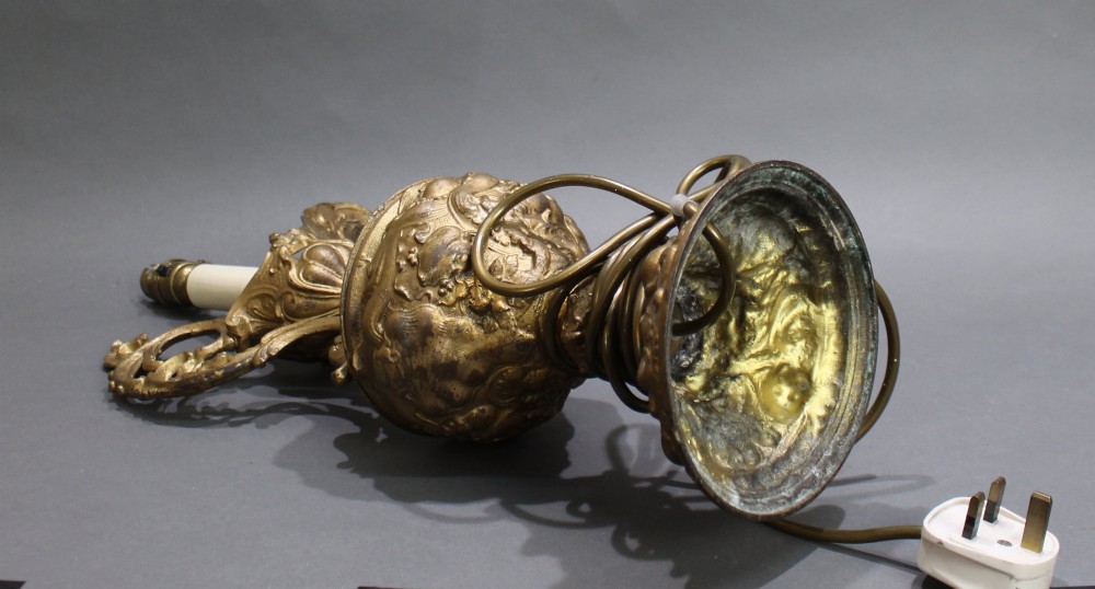 An ornate antique gilt metal table lamp fashioned in the shape of a Rococo ewer with a scrolled handle and intricate leaf relief patterns. View X