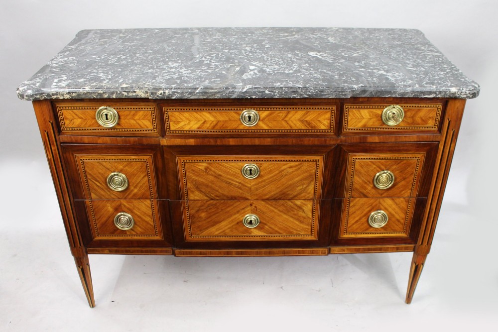 A Louis XVI parquetry commode featuring geometric timber inlays, a grey marble top, brass ring handles, and tapered legs. View II