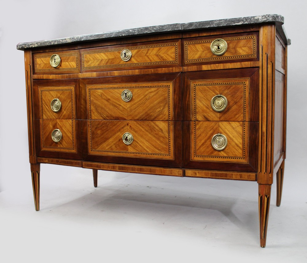 A Louis XVI parquetry commode featuring geometric timber inlays, a grey marble top, brass ring handles, and tapered legs. View III