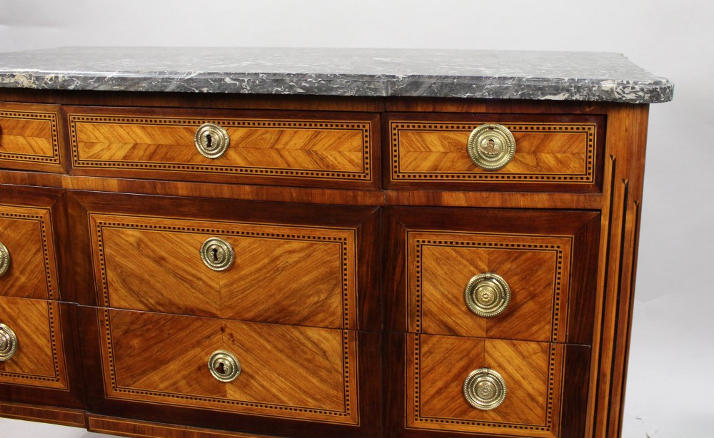 A Louis XVI parquetry commode featuring geometric timber inlays, a grey marble top, brass ring handles, and tapered legs. View V