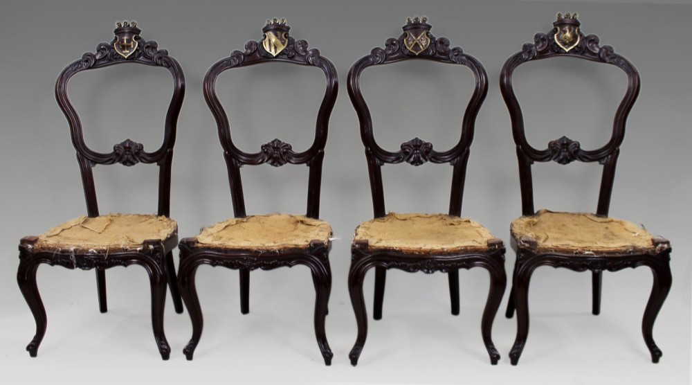 A set of four mid-Victorian dark mahogany side chairs featuring open-carved balloon backs topped with heraldic crest shields and cabriole front legs.