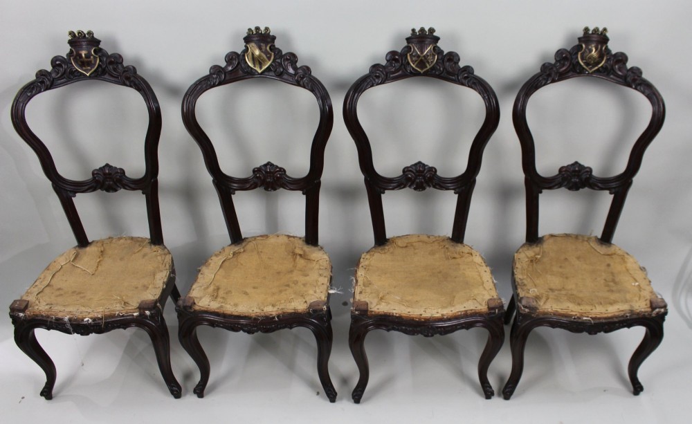 A set of four mid-Victorian dark mahogany side chairs featuring open-carved balloon backs topped with heraldic crest shields and cabriole front legs. View II