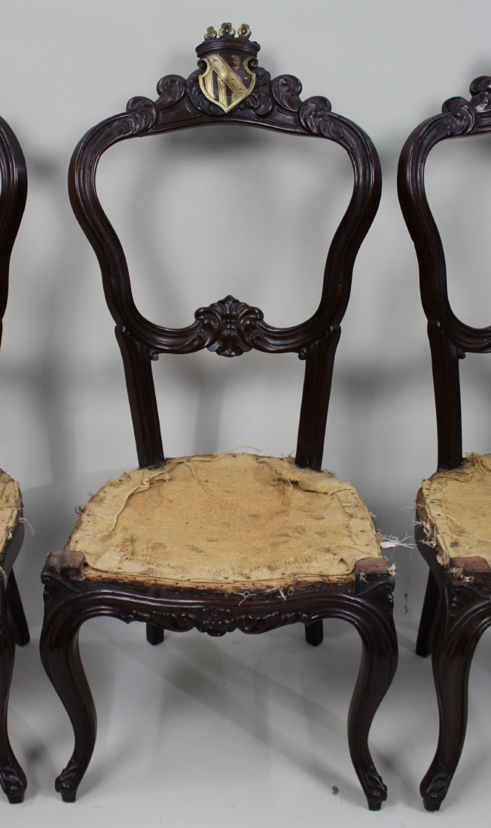 A set of four mid-Victorian dark mahogany side chairs featuring open-carved balloon backs topped with heraldic crest shields and cabriole front legs. View IV