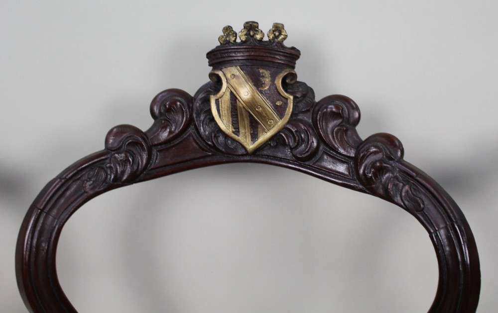 A set of four mid-Victorian dark mahogany side chairs featuring open-carved balloon backs topped with heraldic crest shields and cabriole front legs. View V