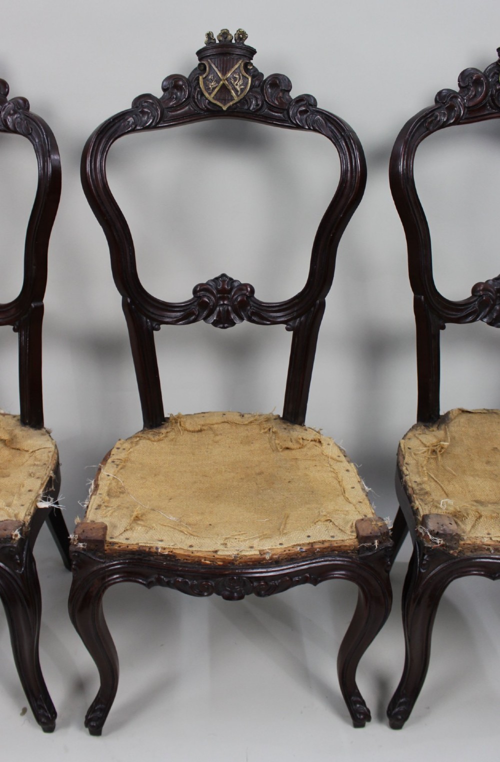 A set of four mid-Victorian dark mahogany side chairs featuring open-carved balloon backs topped with heraldic crest shields and cabriole front legs. View VI