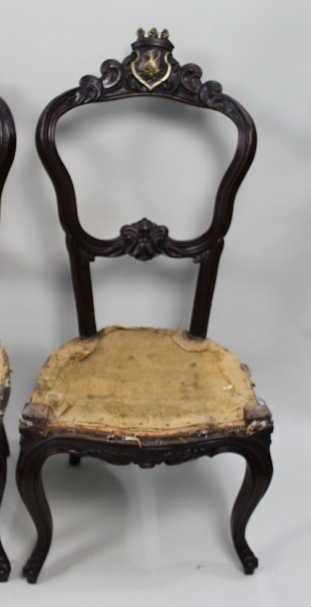 A set of four mid-Victorian dark mahogany side chairs featuring open-carved balloon backs topped with heraldic crest shields and cabriole front legs. View VII