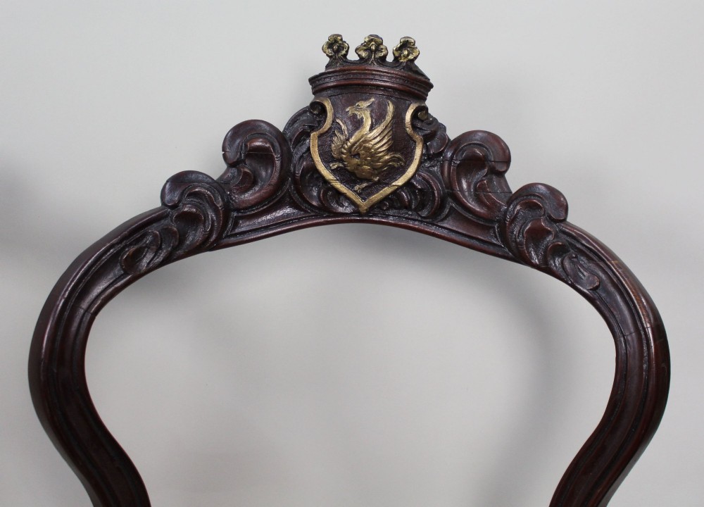 A set of four mid-Victorian dark mahogany side chairs featuring open-carved balloon backs topped with heraldic crest shields and cabriole front legs. View VIII