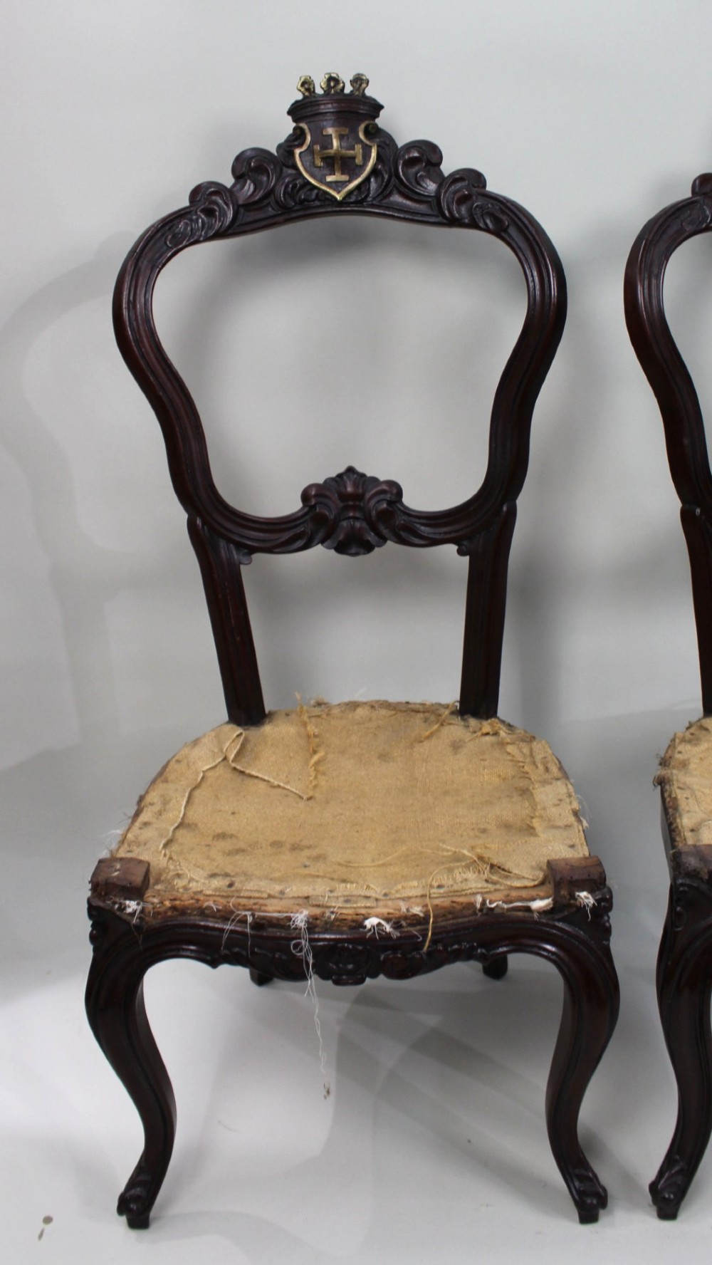 A set of four mid-Victorian dark mahogany side chairs featuring open-carved balloon backs topped with heraldic crest shields and cabriole front legs. View X