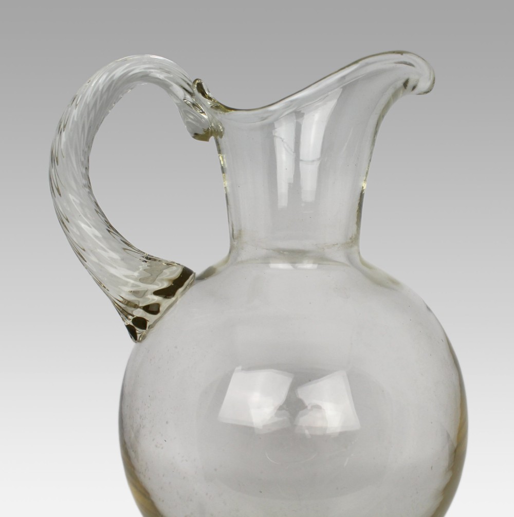 A late 19th-century Italian hand-blown clear glass footed ewer featuring a spherical body, pinched spout, applied ribbed handle, and twisted stem on a flat circular base. View IV