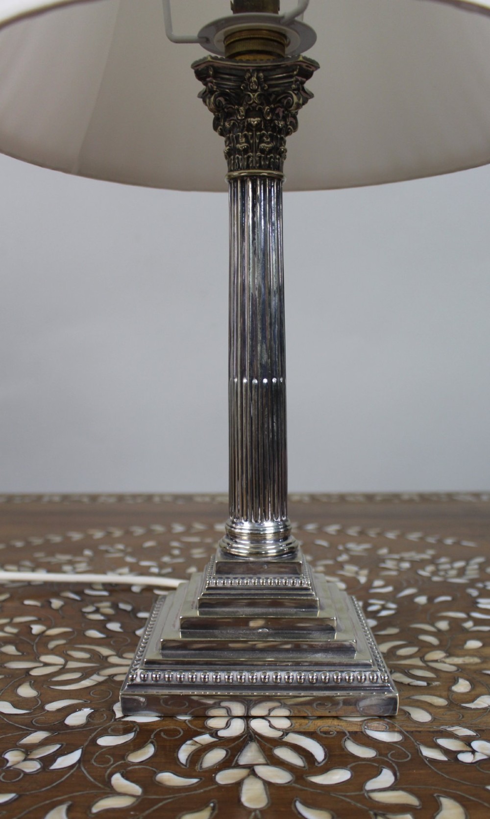 A silver-plated table lamp featuring a fluted Corinthian column shaft, a stepped square base, and a cream pleated fabric shade. View II