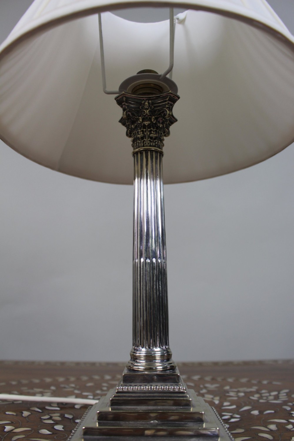 A silver-plated table lamp featuring a fluted Corinthian column shaft, a stepped square base, and a cream pleated fabric shade. View III