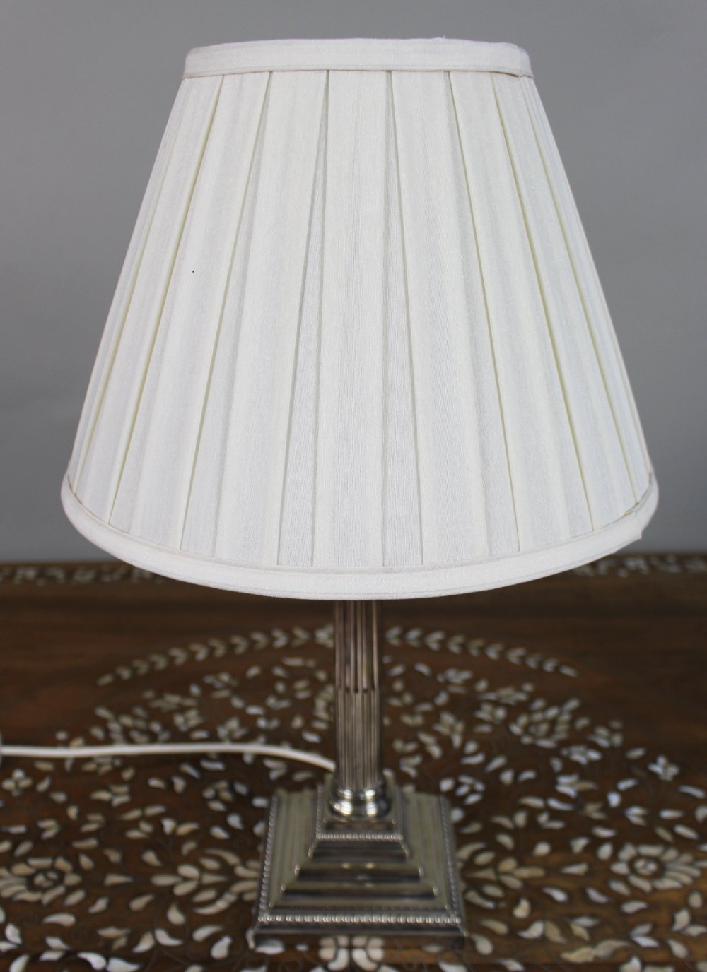 A silver-plated table lamp featuring a fluted Corinthian column shaft, a stepped square base, and a cream pleated fabric shade. View IV
