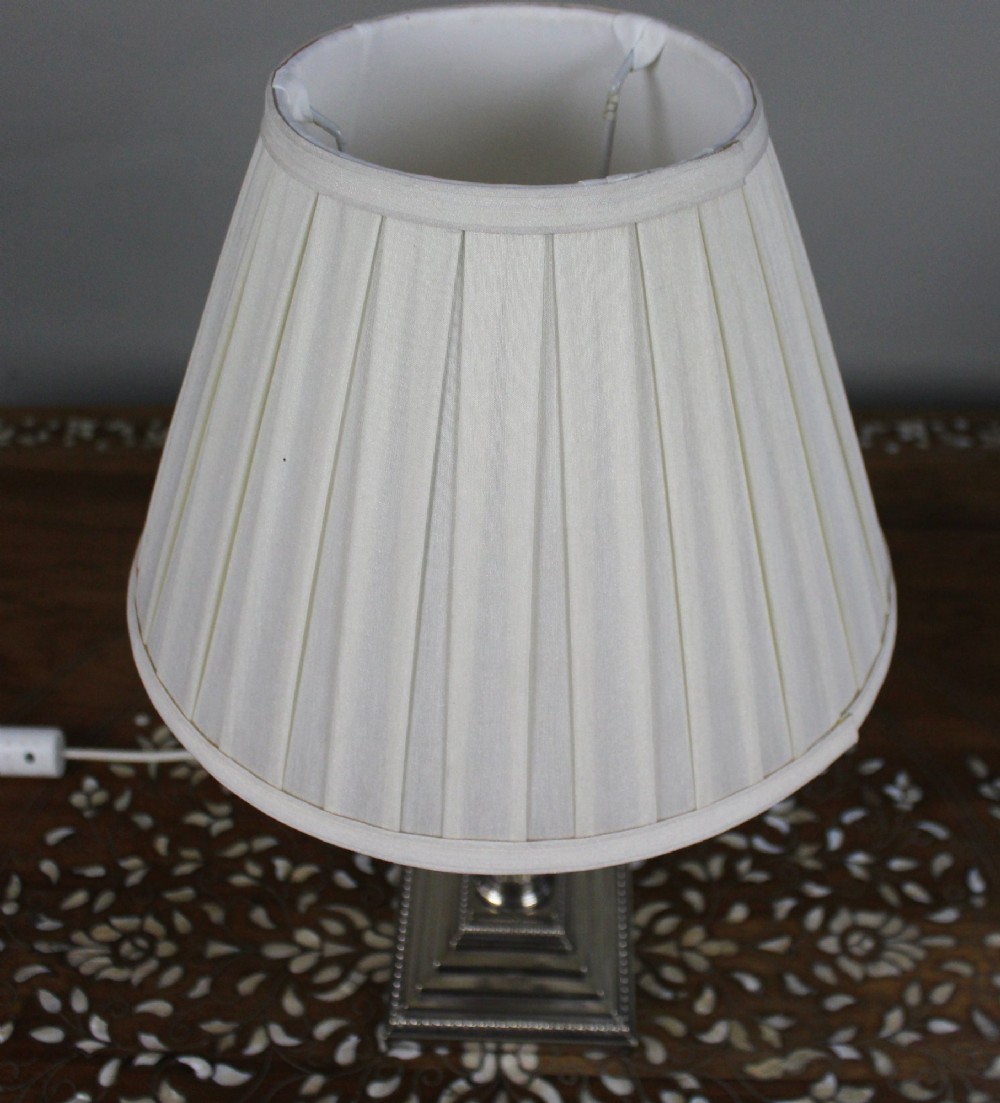 A silver-plated table lamp featuring a fluted Corinthian column shaft, a stepped square base, and a cream pleated fabric shade. View V