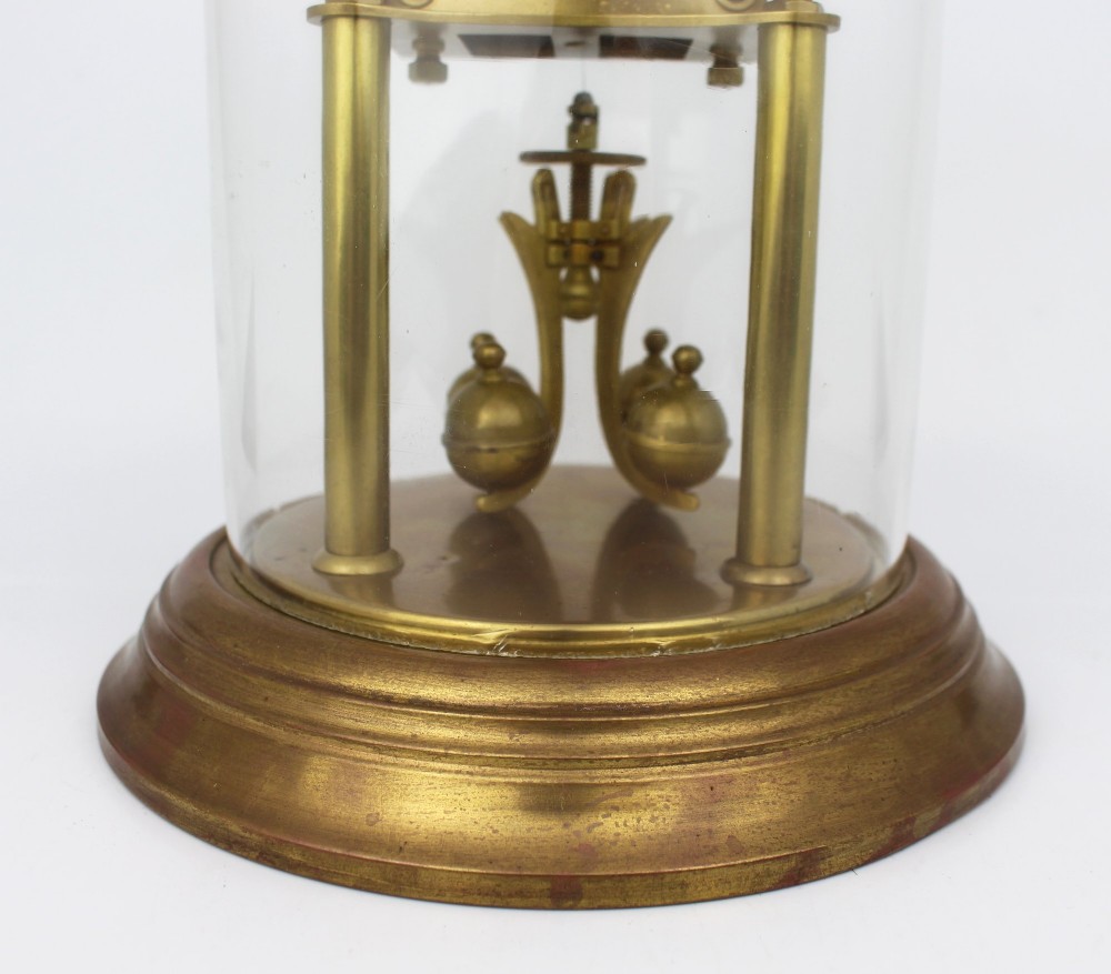 An antique German anniversary clock featuring a brass movement and four-ball rotary pendulum enclosed under a clear glass dome. View IV