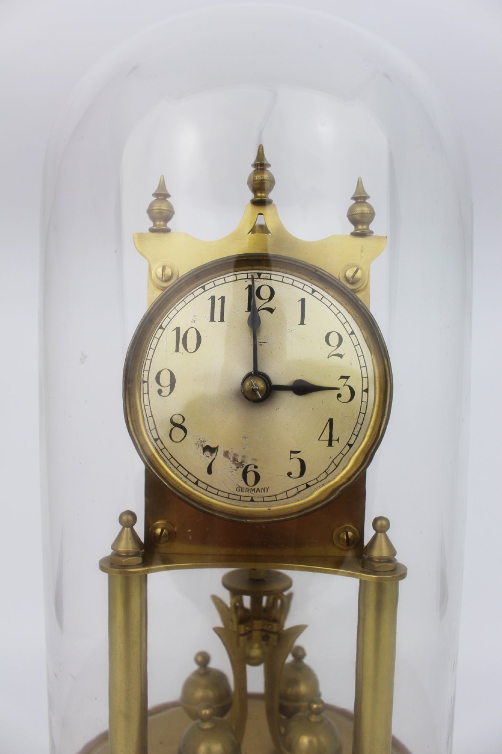 An antique German anniversary clock featuring a brass movement and four-ball rotary pendulum enclosed under a clear glass dome. View V