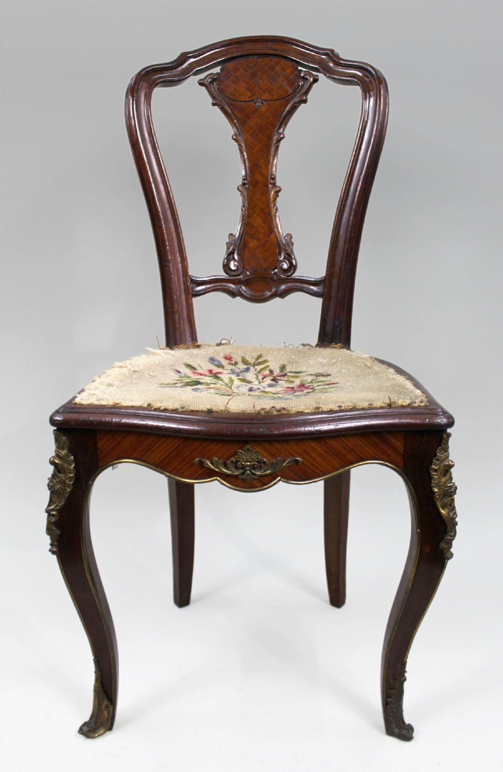 An antique French side chair featuring a kingwood back frame with a parquetry splat, cabriole front legs decorated with ormolu mounts, and a floral needlepoint seat.