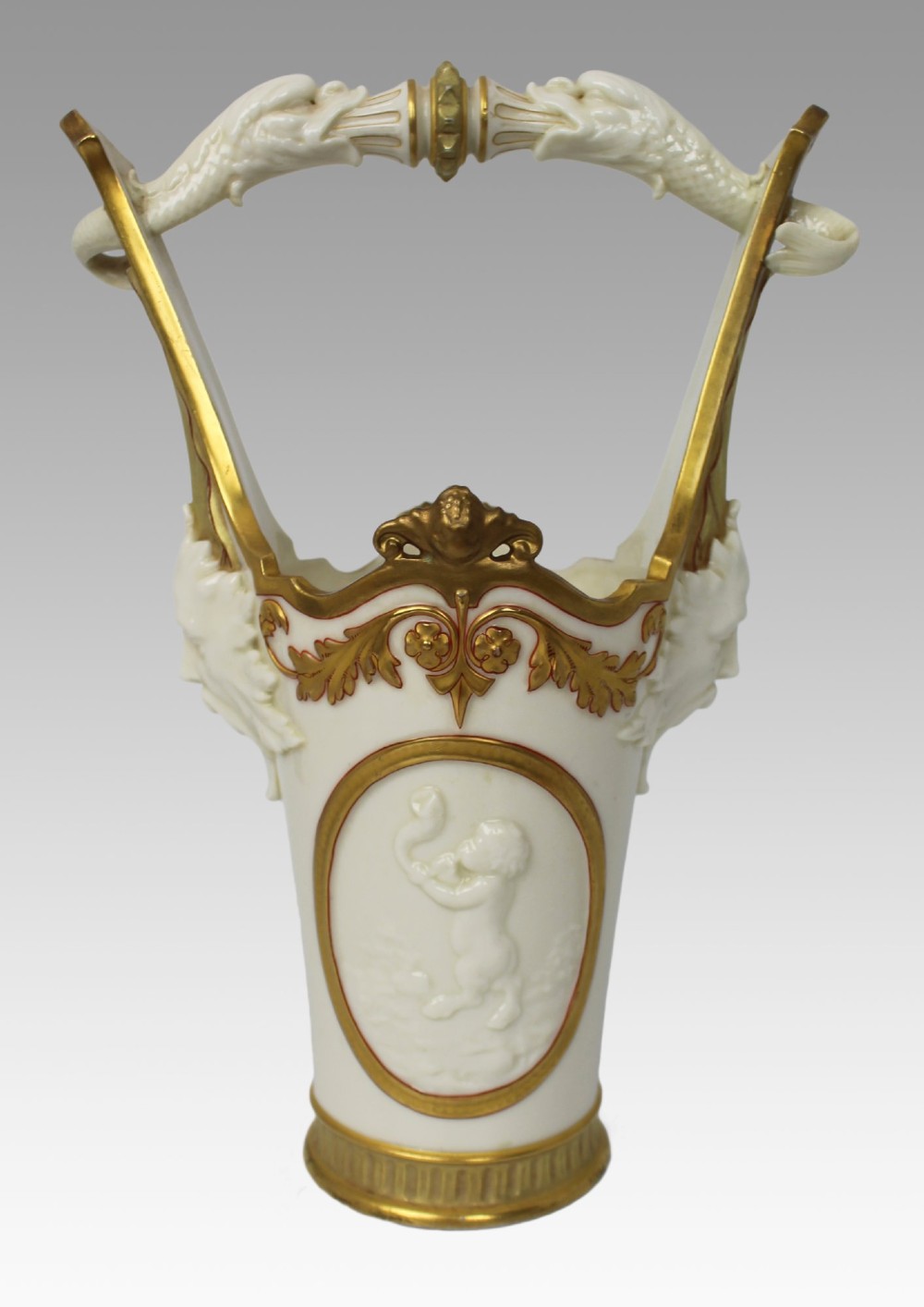 A white porcelain vase featuring a central white relief medallion of a cherub, gold gilded borders, raised side mask faces, and an overhead dolphin handle. View XI